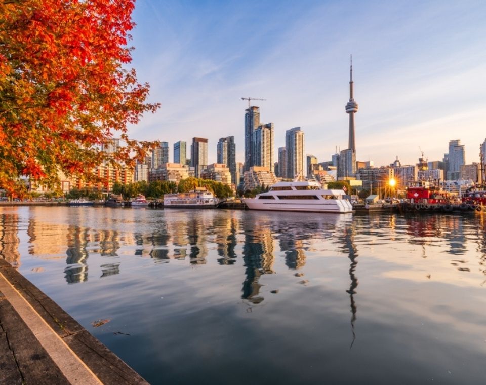 Toronto mit CN Tower, Hochhäusern und Ausflugsschiffen am Wasser, eingerahmt von leuchtend rot-orangefarbenem Herbstlaub Kanada-Rundreise