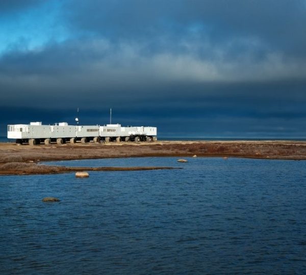 Ein weißer Tundra Buggy steht an der Küste der Hudson Bay bei Churchill unter dunklen Wolken und am Wasser. Kanada-Rundreise